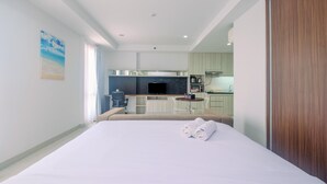 A hotel room with a large bed, a desk, and a kitchenette in the background. - Stunning Studio Azalea Suites Apartment (Cikarang)