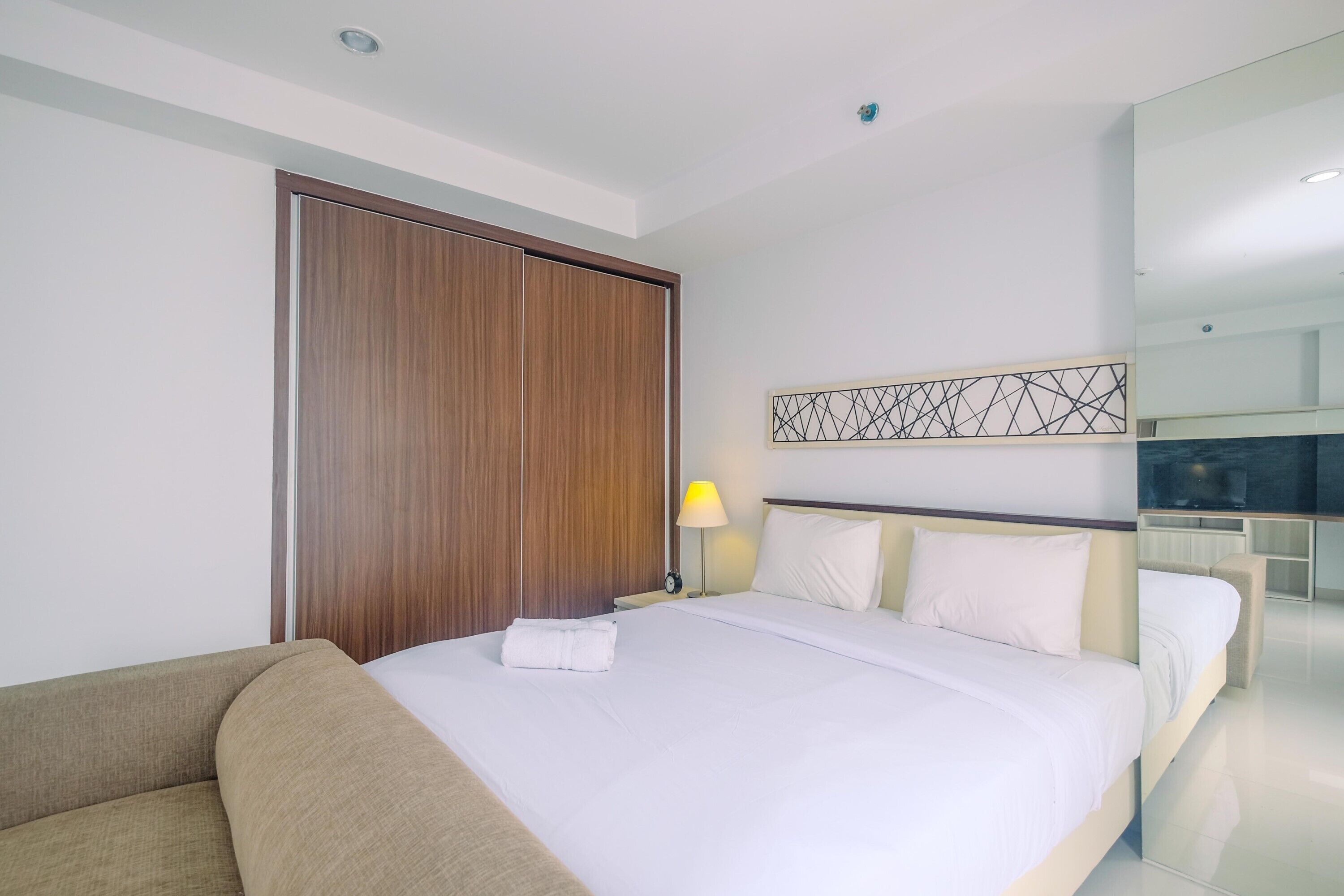 Une chambre d’hôtel comprenant un lit, un canapé, une armoire en bois, un téléviseur fixé au mur et une table de chevet avec une lampe.