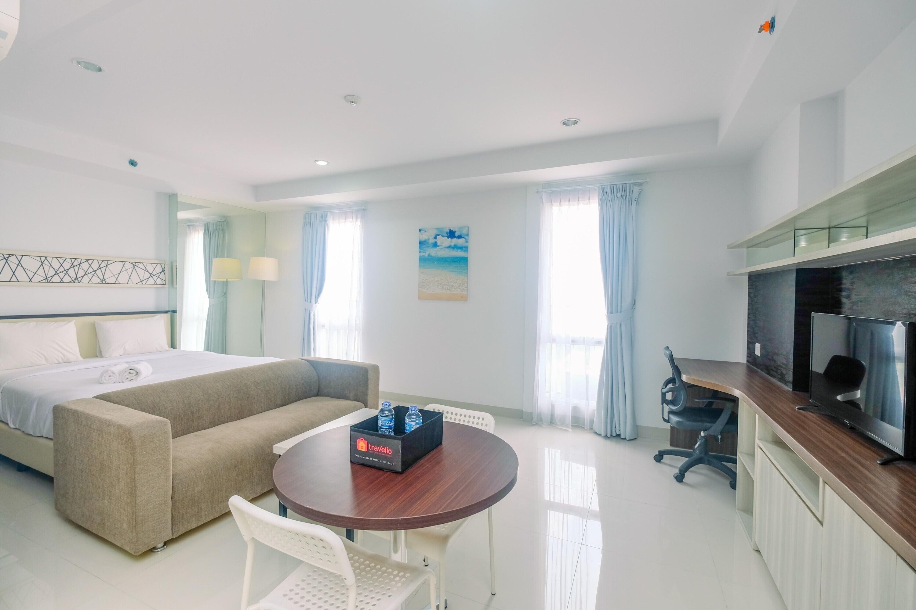 Ein modernes Hotelzimmer mit Bett, Sofa, Esstisch, Fernseher und einer kleinen Küchenzeile.