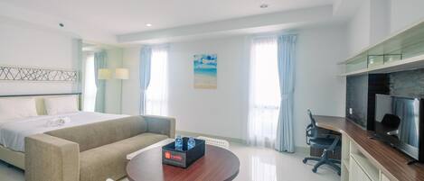 Ein modernes Hotelzimmer mit Bett, Sofa, Esstisch, Fernseher und einer kleinen Küchenzeile.
