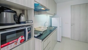 A modern kitchen with a microwave, kettle, and coffee maker on the countertop, a built-in oven, and a refrigerator. - Stunning Studio Azalea Suites Apartment (Cikarang)