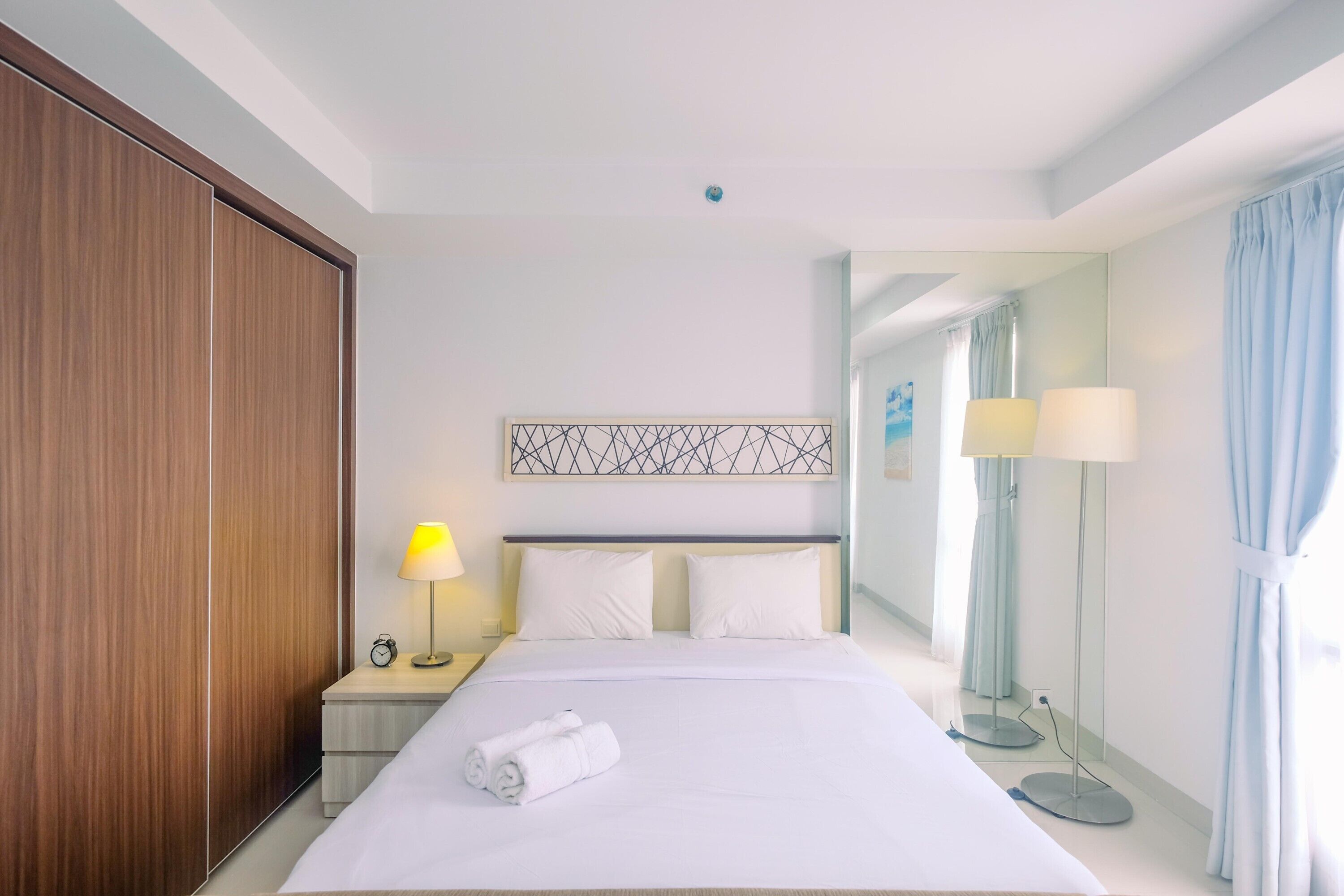 A hotel room with a large bed, a wooden wardrobe, a nightstand with a lamp, and a mirror.