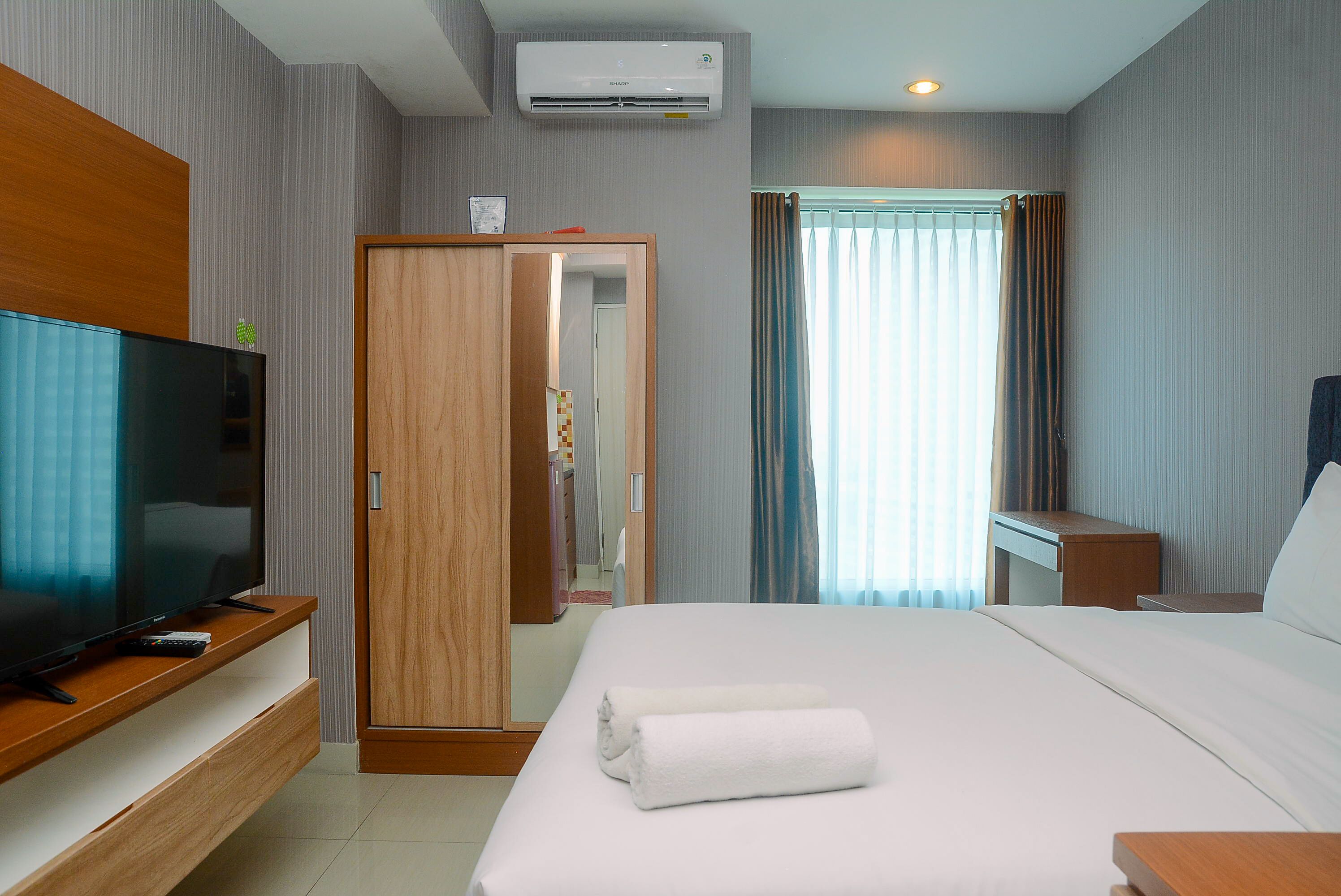 Ein Hotelzimmer mit Bett, Fernseher auf einem Holztischchen, Kleiderschrank und einem Fenster mit Vorhängen.