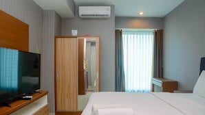 Camera d'albergo con un letto, una televisione su un supporto in legno, un armadio e una finestra con tende.