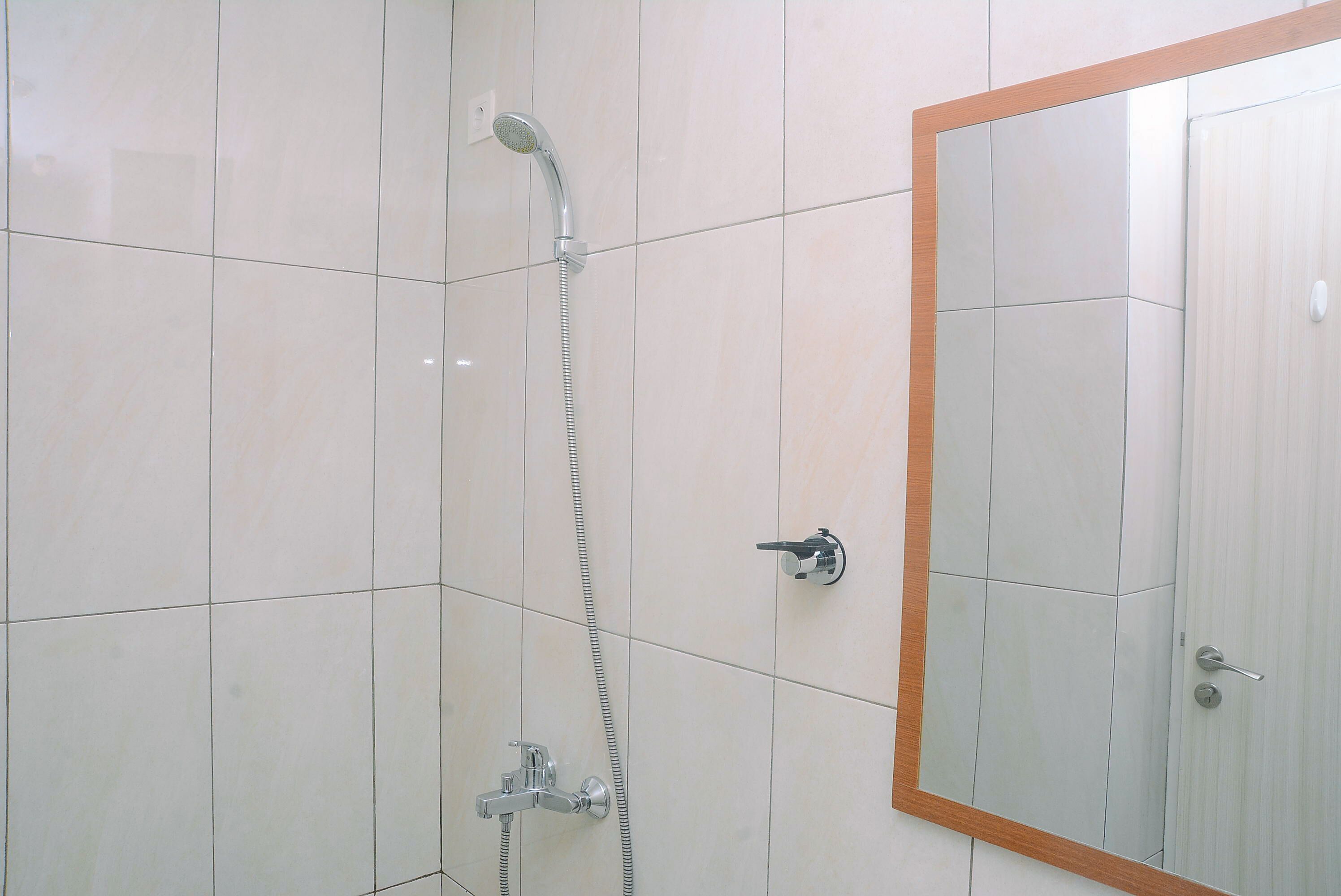 Un bagno con piastrelle bianche, una doccia con soffione a mano e uno specchio con cornice in legno.