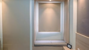 Un couloir étroit avec une porte fermée, un petit banc et un tableau encadré accroché au mur.