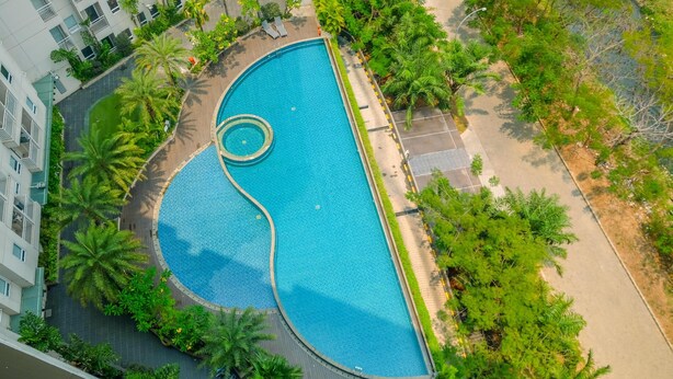 Vue aérienne d’une piscine entourée de palmiers et bordée d’une allée pavée.
