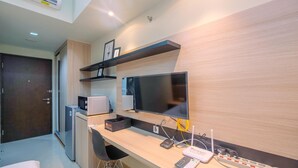 Une chambre d’hôtel moderne équipée d’un bureau en bois, d’un téléviseur à écran plat, d’un mini-réfrigérateur, d’un four à micro-ondes et d’une multiprise.