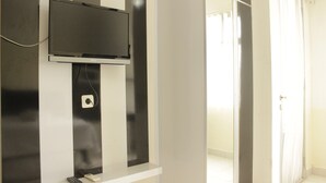 A modern room with a mounted flat-screen TV, a small shelf with a remote control, and a door leading to another area.