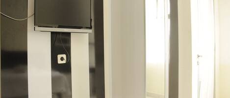 A modern room with a mounted flat-screen TV, a small shelf with a remote control, and a door leading to another area.