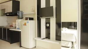 A compact hotel room with a kitchenette, a bed, and a TV mounted on the wall.