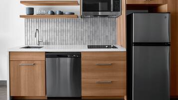 Une cuisine moderne avec des meubles en bois, un lave-vaisselle en acier inoxydable, un réfrigérateur noir et un four à micro-ondes.