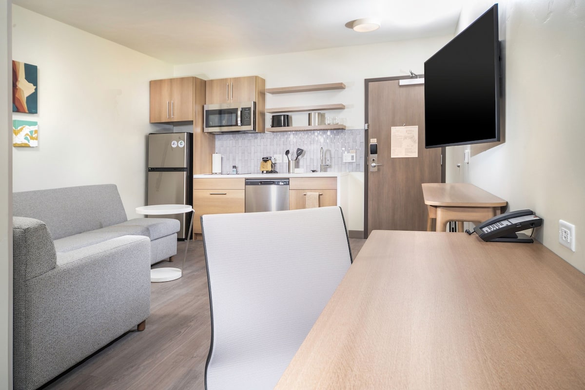 A compact kitchen with modern appliances, a dining area with a table and chairs, and a flat-screen TV mounted on the wall.