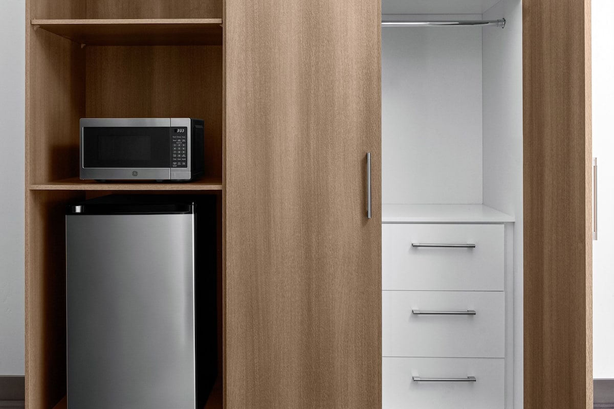 A kitchen with a microwave on a shelf, a refrigerator, and a white cabinet with drawers.