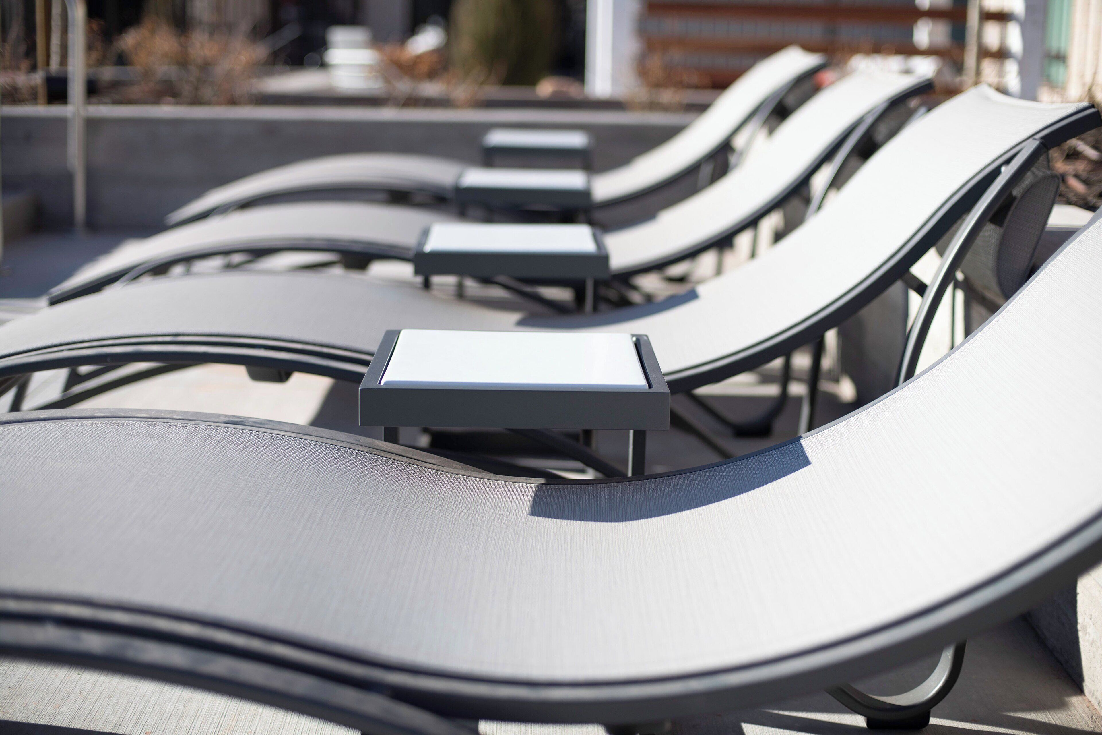 A row of sun loungers with metal frames and fabric seats, arranged outdoors.