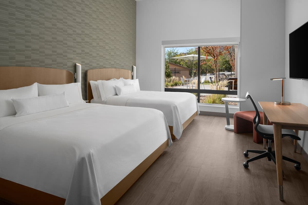 A hotel room with two beds, a desk, a chair, and a TV.