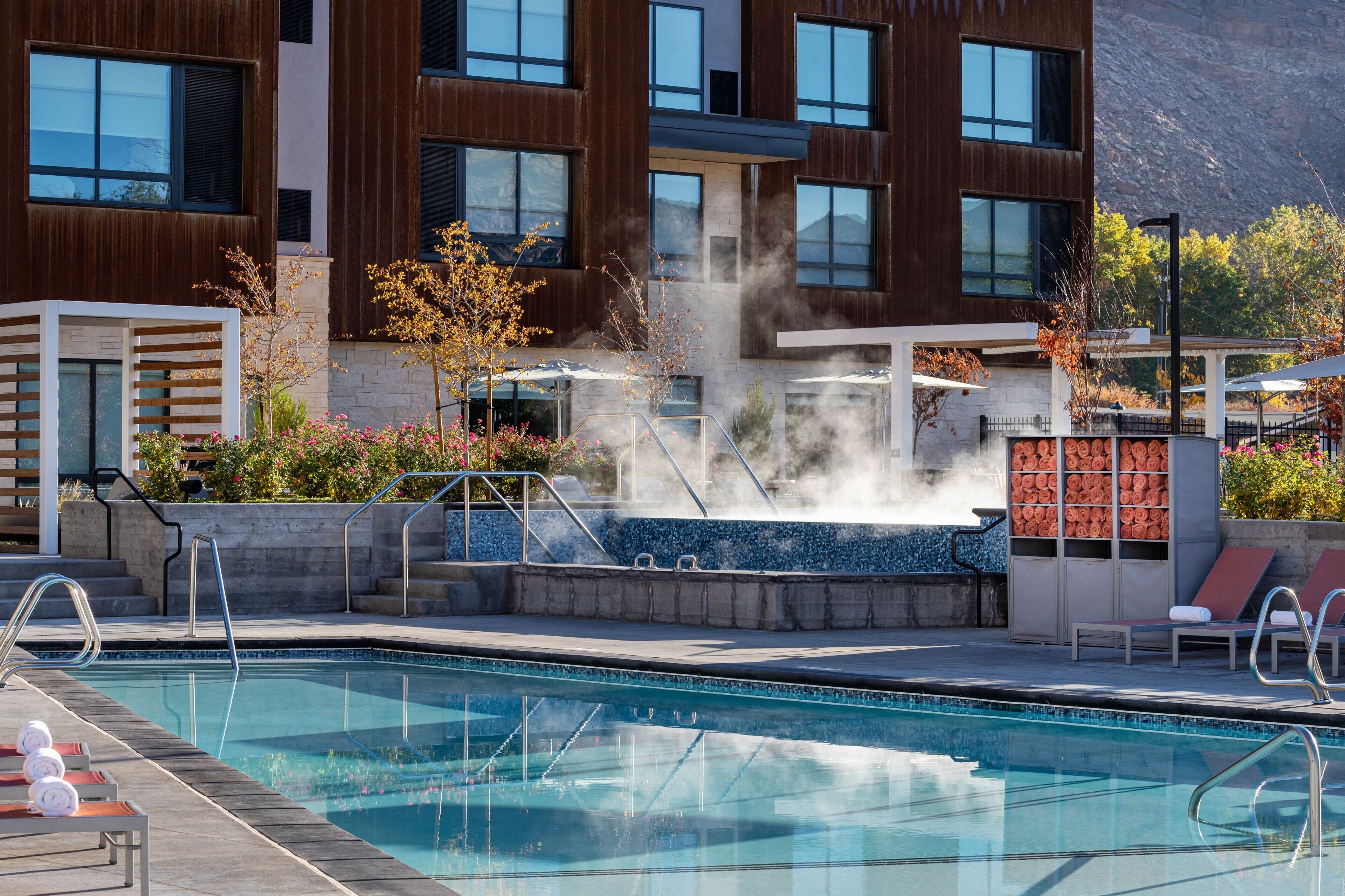 A modern hotel with a swimming pool, outdoor seating, and a steam feature.