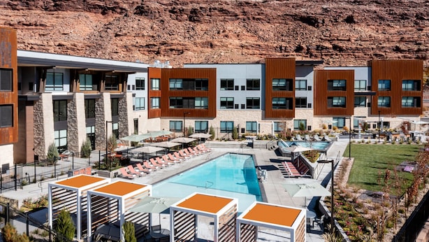 Un hotel con piscina, mobiliario exterior y montañas al fondo.