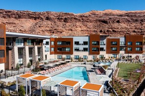 Un hotel con piscina, mobiliario exterior y montañas al fondo.