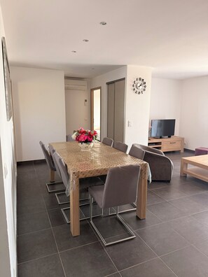 Un salon moderne comprenant une table à manger, un canapé, un téléviseur et une horloge murale.