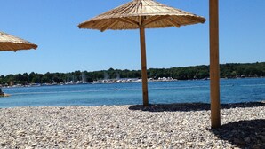 A pebbled beach with thatched umbrellas and a clear view of the sea and distant trees. - Studio apartment Sweetie with pool (Funtana)