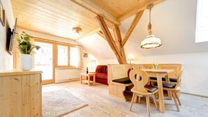 Een houten interieur met een eettafel en stoelen, een bank en een groot raam.