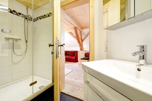 Un baño con ducha, lavamanos y vigas de madera en el techo.