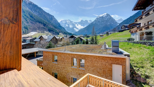 Uitzicht vanaf een houten balkon op een bergdorp met traditionele gebouwen en een heldere lucht.