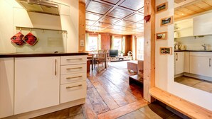 Een keuken met houten kasten, een eethoek met een tafel en stoelen, en een televisie.