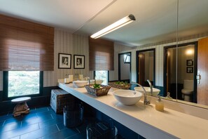 Un baño moderno con un espejo grande, dos lavamanos y un ventanal con persianas.