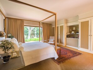 Un dormitorio amplio con una cama grande, un sillón, un armario y vistas al verdor exterior.
