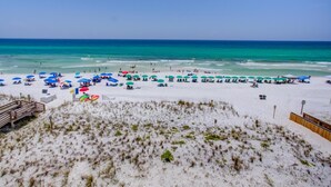 Een strand met talloze parasols en ligbedden, een houten vlonder en een grasachtig duinlandschap.