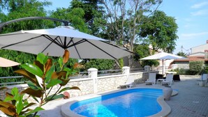 A swimming pool with lounge chairs and umbrellas, surrounded by a stone wall and greenery. - Vacation apartment Torana in Funtana with pool (Funtana)