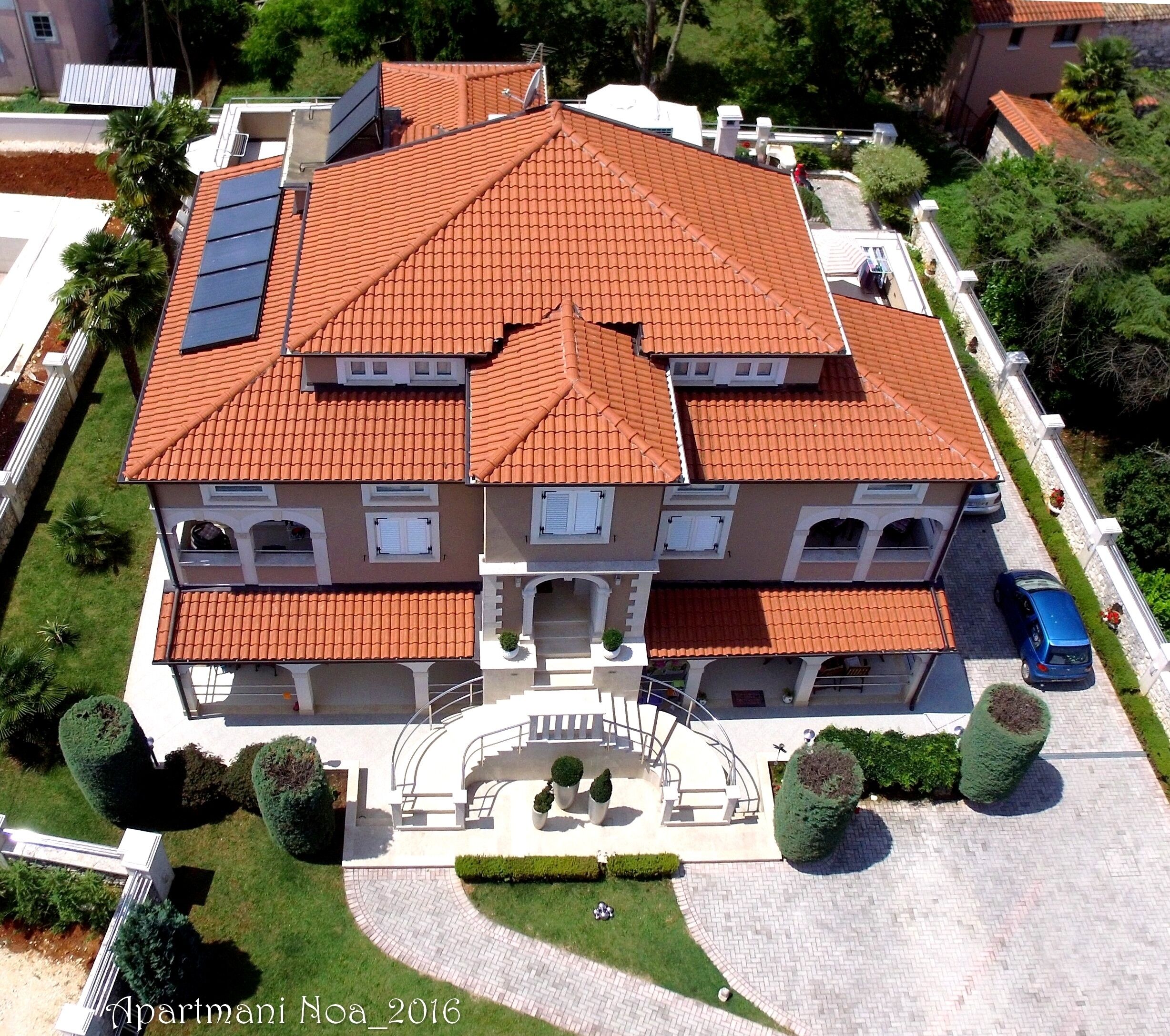 A multi-story building with a red-tiled roof, a central staircase, and a paved driveway.