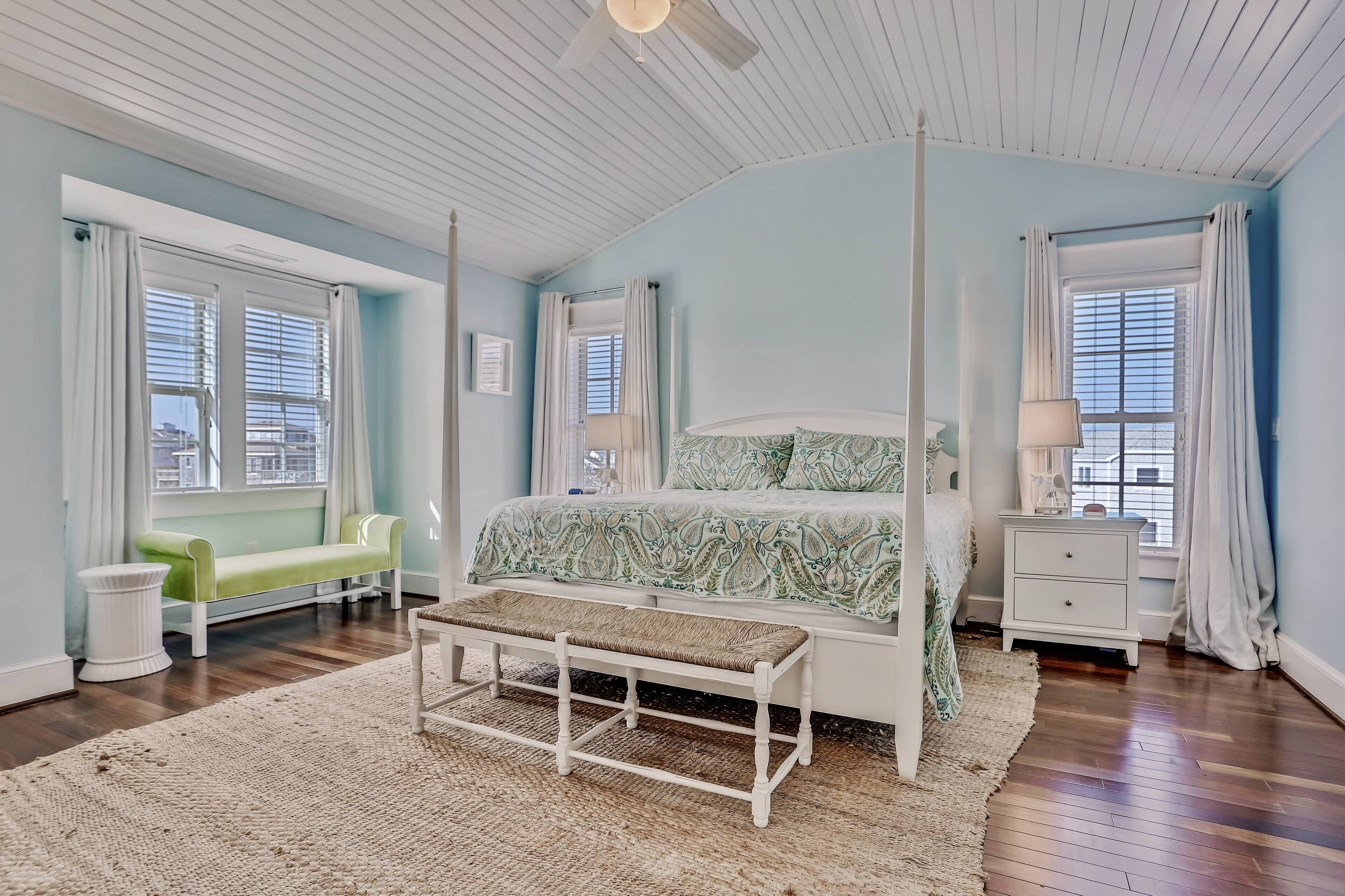 A bedroom with a four-poster bed, a bench, a nightstand, and a green bench by the window.