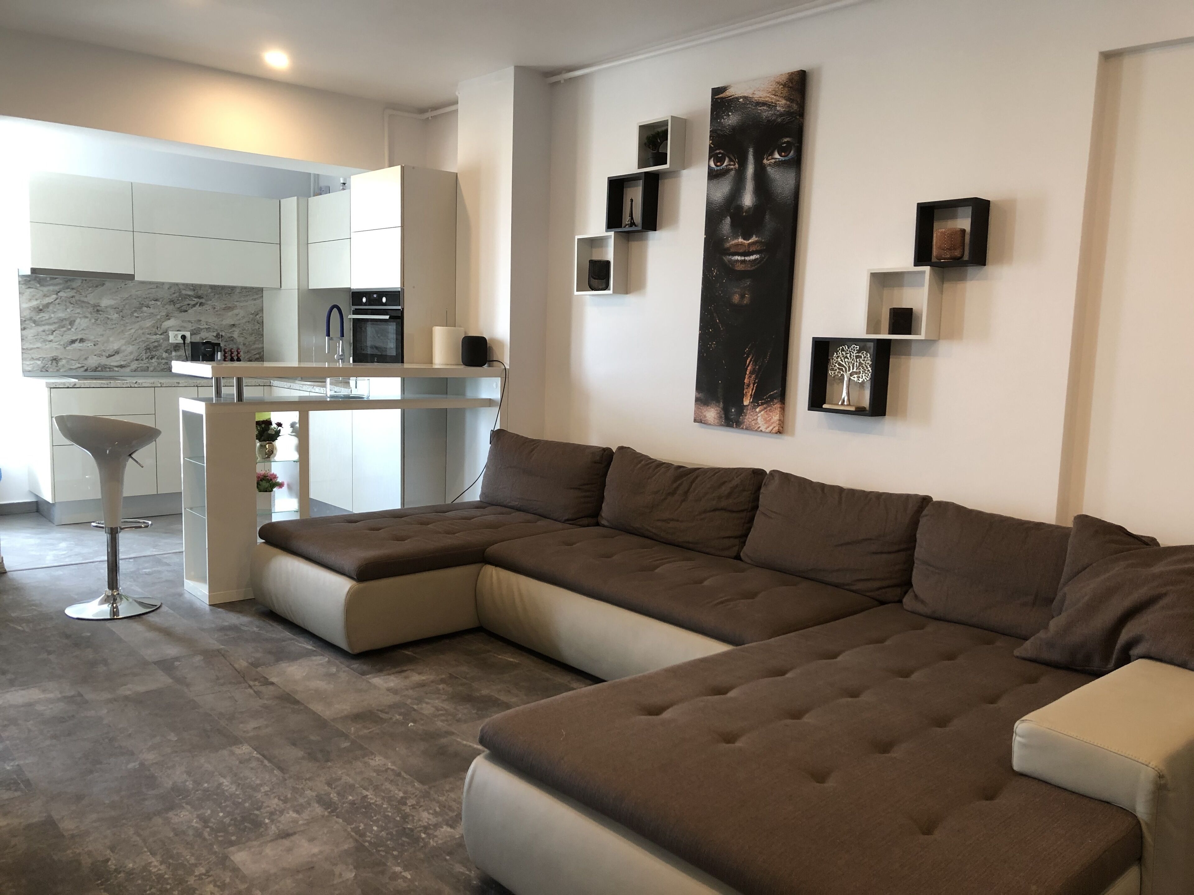 A modern living room with a sectional sofa, a kitchen area with white cabinets, and a marble backsplash.