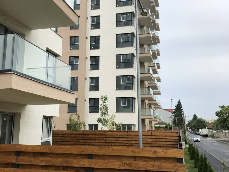 A multi-story residential building with balconies, a street view, and a wooden fence.