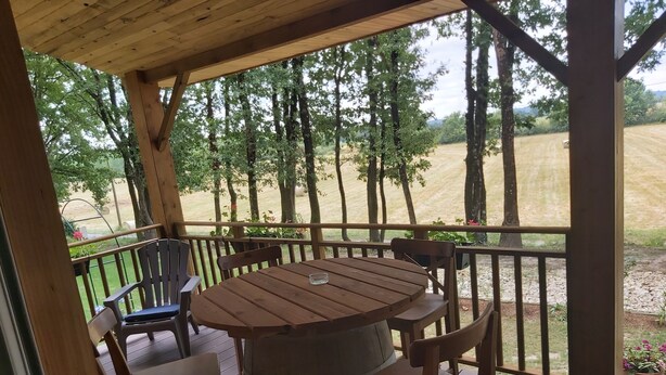 A wooden deck with a round table and four chairs, overlooking a grassy area with trees. - Le gîte du Pic-vert in the woods of Périgord Pourpre (Saint-Pierre-d'Eyraud)