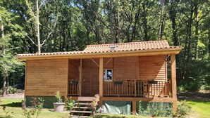 A wooden cabin with a tiled roof, a porch with seating, and a small window. - Le gîte du Pic-vert in the woods of Périgord Pourpre (Saint-Pierre-d'Eyraud)