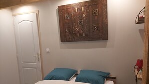 A bedroom with a bed, teal pillows, a white duvet, a wooden headboard, a white door, and a wall-mounted artwork. - Le gîte du Pic-vert in the woods of Périgord Pourpre (Saint-Pierre-d'Eyraud)