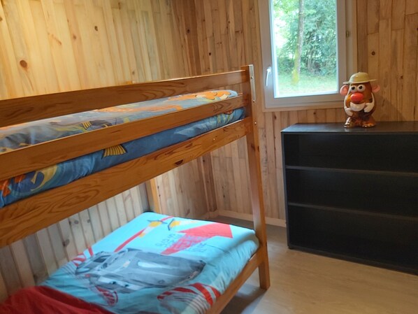 Ein Stockbett mit bunter Bettwäsche, eine hölzerne Kommode und eine Spielzeugfigur.
