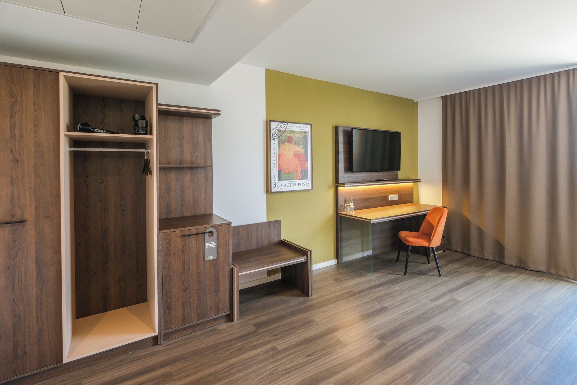 Habitación de hotel con armario de madera, escritorio con silla, televisor de pantalla plana y un ventanal con cortinas.