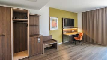 Habitación de hotel con armario de madera, escritorio con silla, televisor de pantalla plana y un ventanal con cortinas.