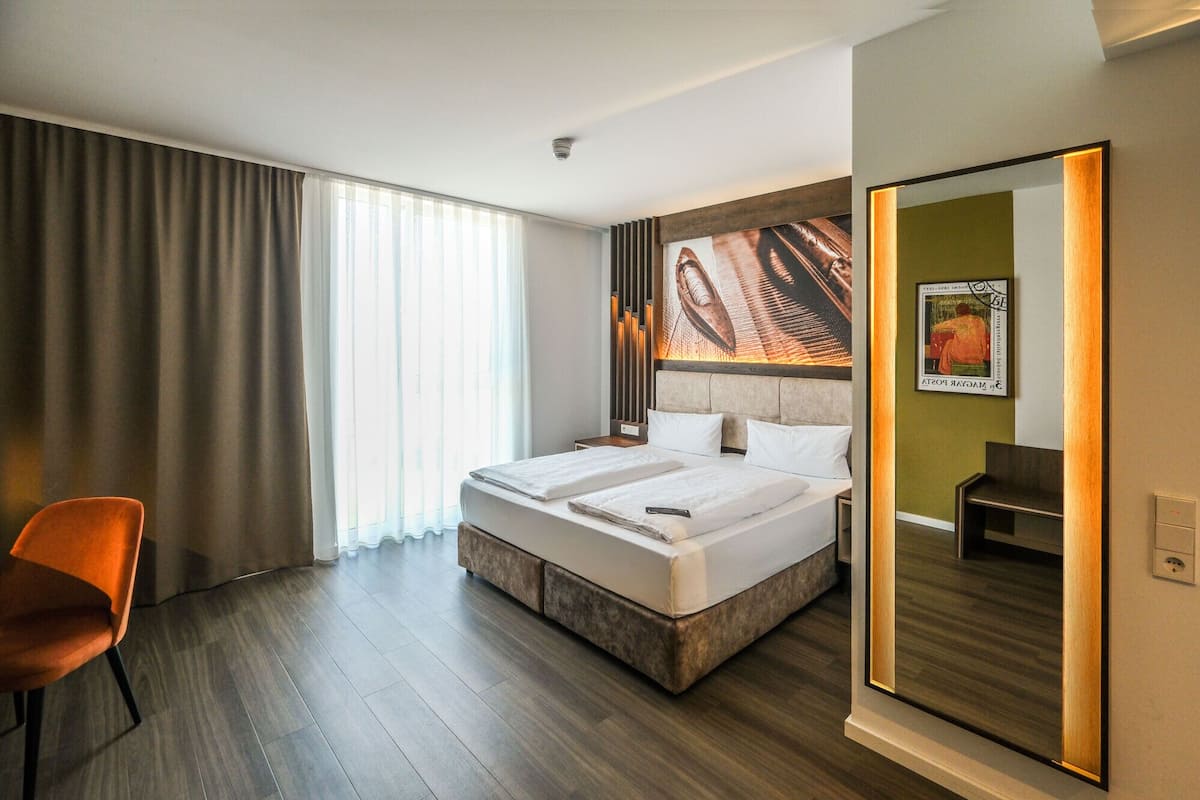 Une chambre d’hôtel avec un grand lit, une chaise, un miroir et un tableau au mur.
