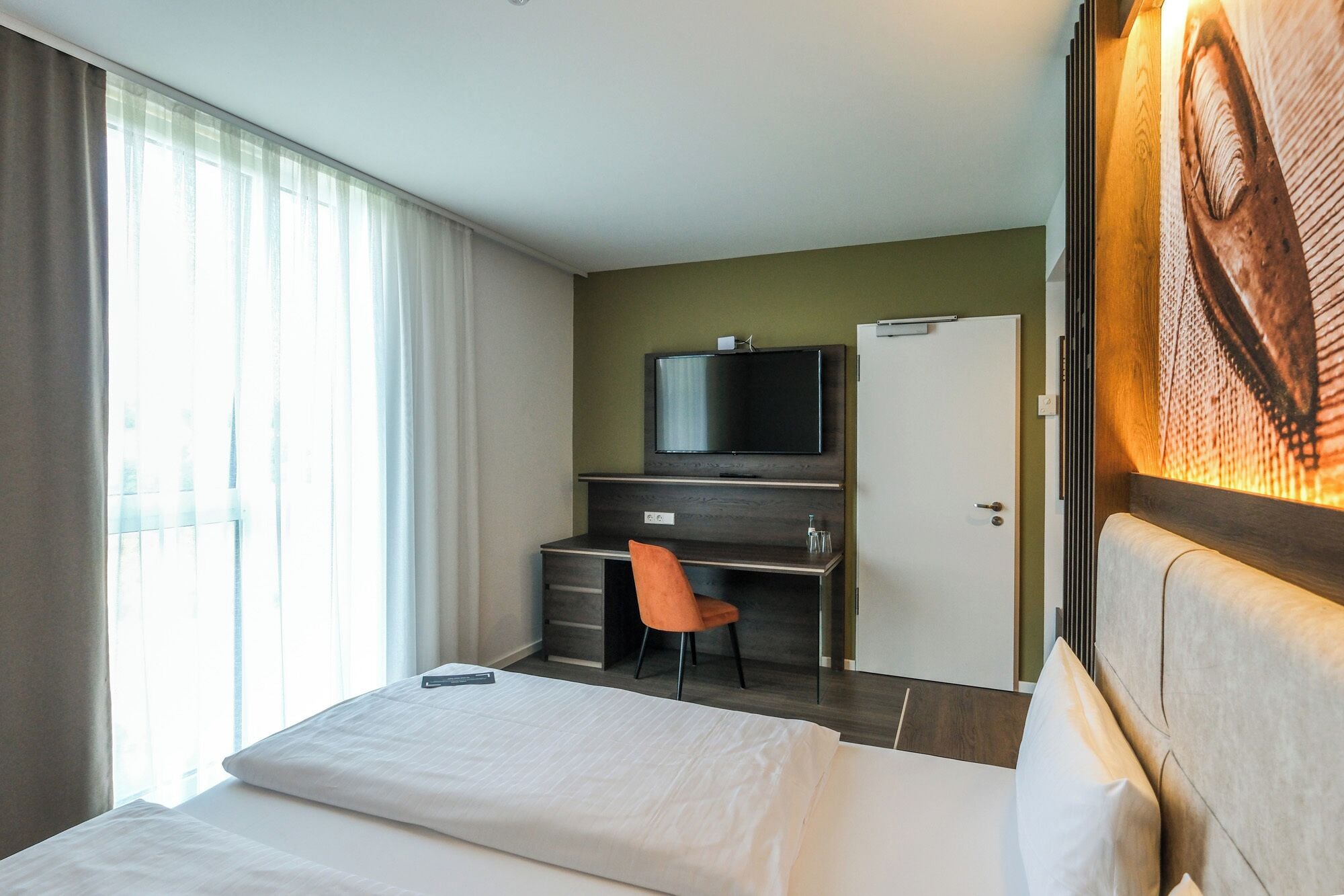 A hotel room with a bed, a desk with a chair, a television, and a door.