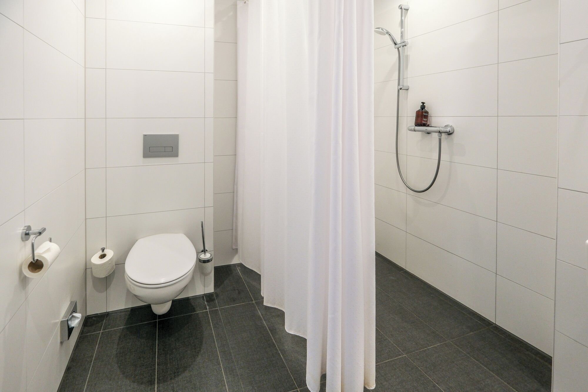 Un baño moderno con inodoro, ducha y dispensador de papel higiénico.