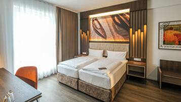 Ein Hotelzimmer mit einem Doppelbett, einem Schreibtisch mit zwei Stühlen, einem großen Fenster mit Vorhängen und einem Wandbild.