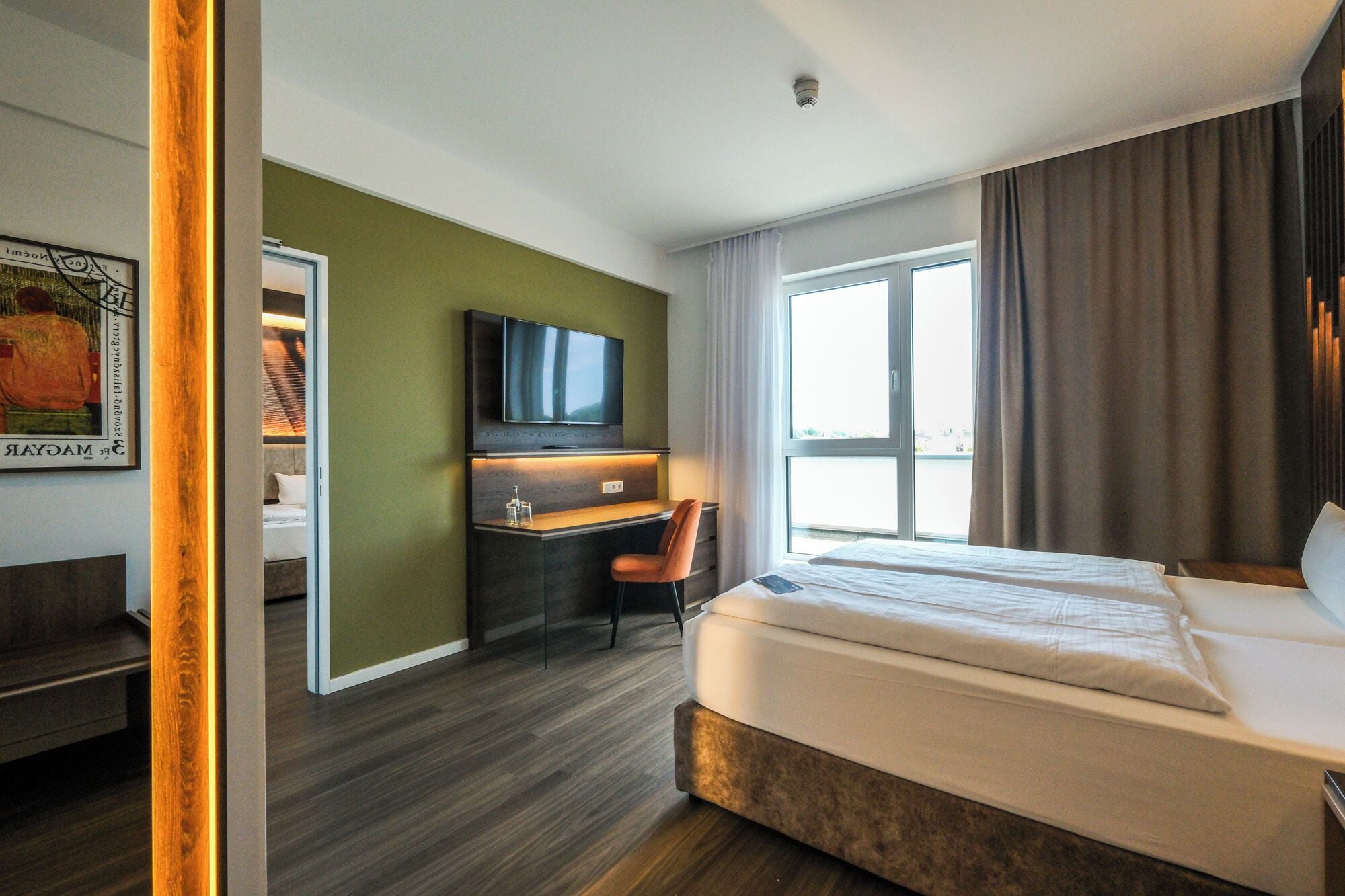 Habitación de hotel con una cama, un escritorio con una silla, un televisor y un ventanal con cortinas.