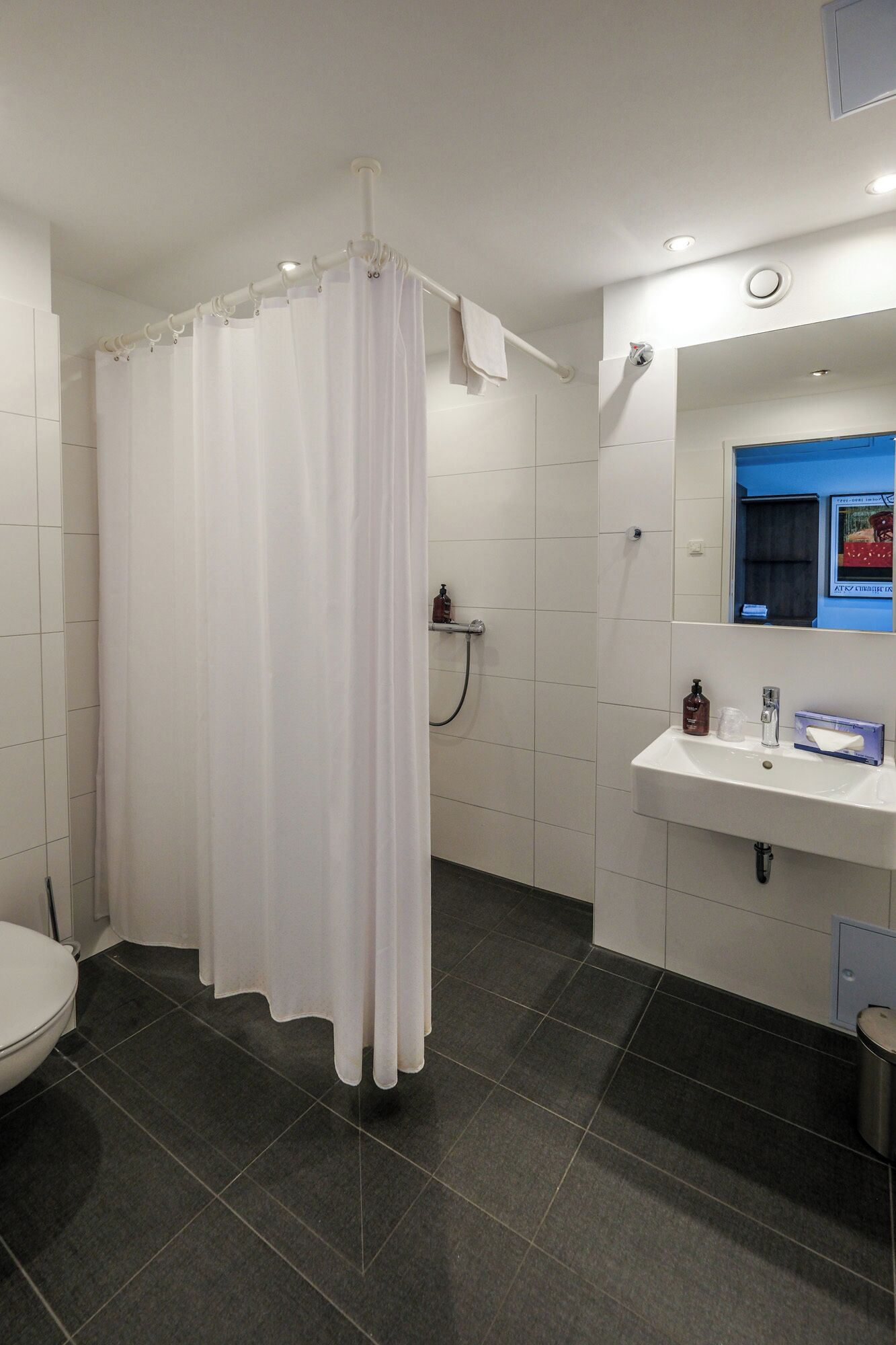 A bathroom with a white shower curtain, a white sink with toiletries, and a mirror above the sink.