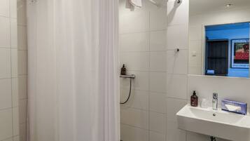 A bathroom with a white shower curtain, a white sink with toiletries, and a mirror above the sink.